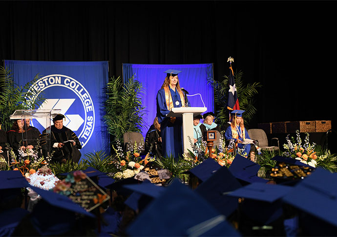 Graduate in cap and gown stands on stage and address crowd