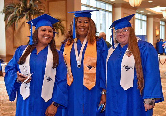 Three graduates in cap and gown pose at graduation.