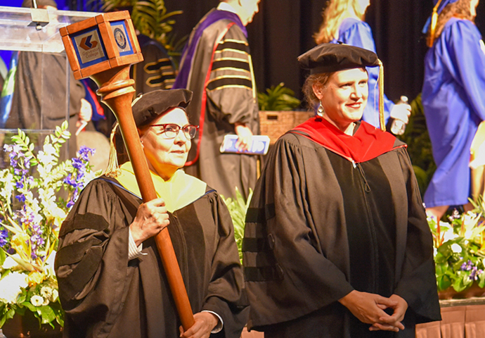 Two women in cap and gown participate in graduation ceremony.