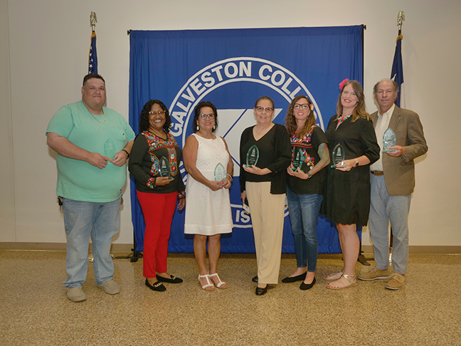 Employees stand with their awards in front of Galveston College flag.