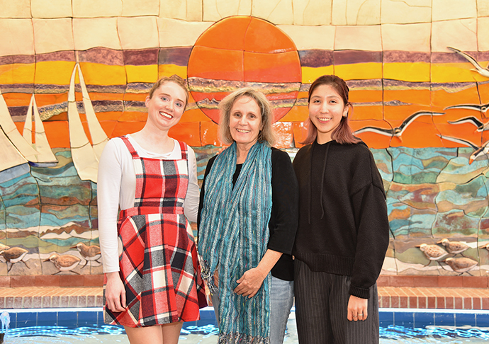 Two students pose with PTK Chapter President in front of colorful sunset mural.
