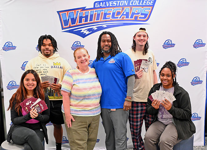 6 people stand in front of Whitecaps backdrop, holding gift cards. 