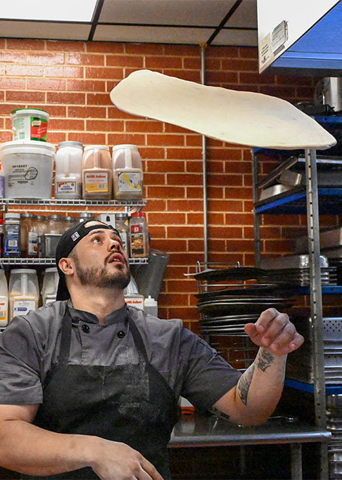 Person tosses pizza dough into air in kitchen