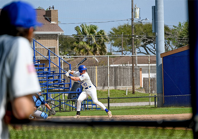 Coach watches as baseball player swings at pitch