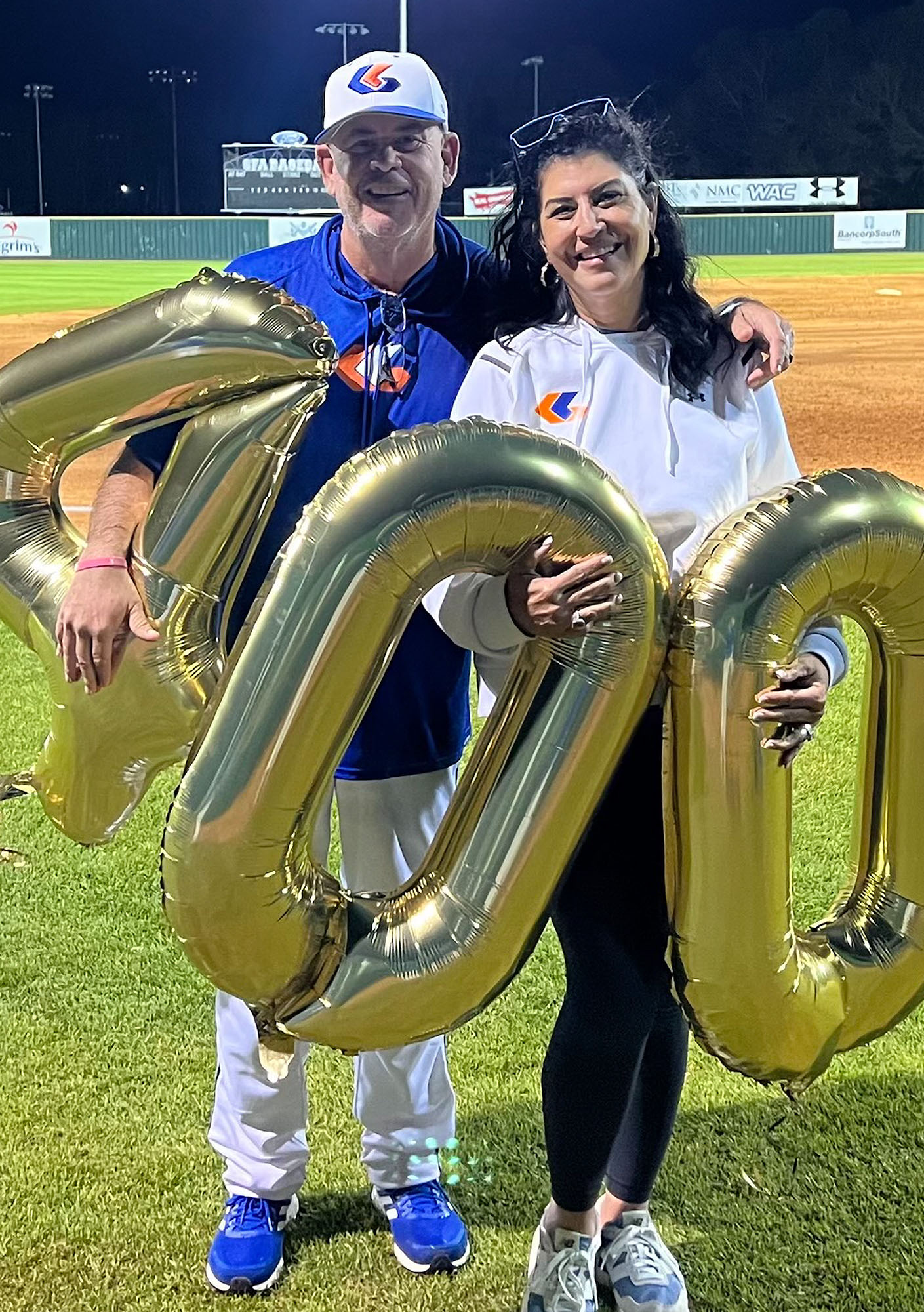 Two people on a baseball field holding balloons that say 400