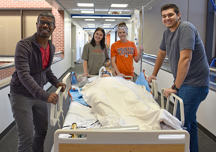 4 health care students with a test patient dummy on a hospital bed.