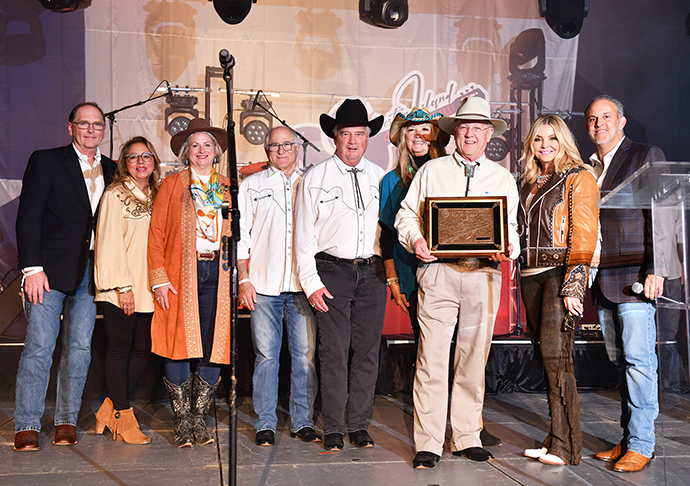 9 people stand on stage posing with award plaque.
